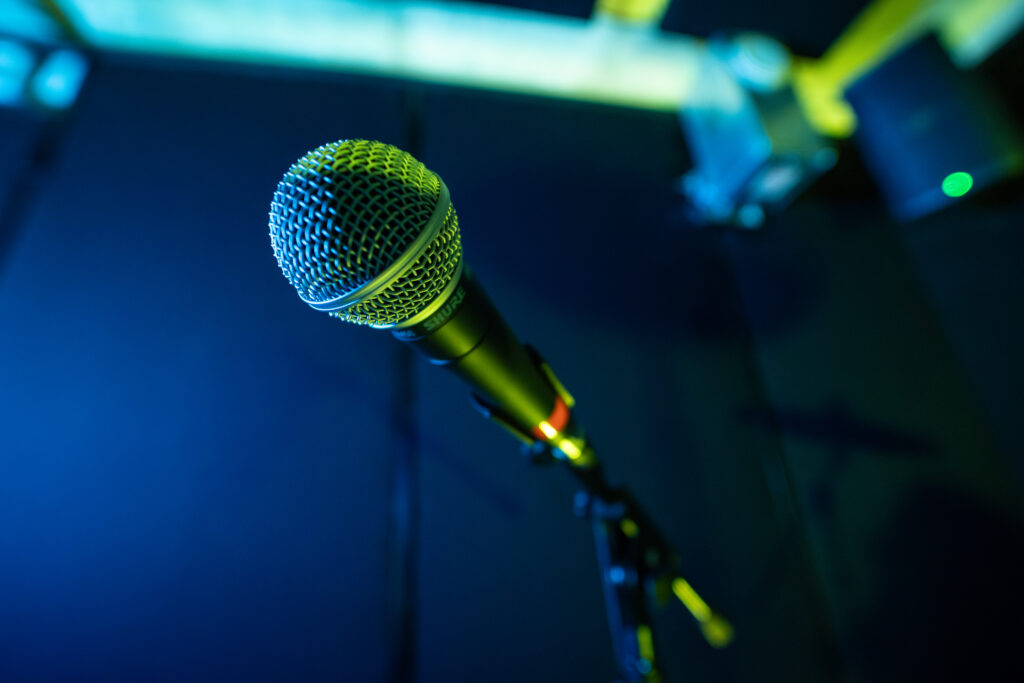 Close-up of a Shure microphone on a stand inside a Band Barracks rehearsal studio, illuminated with blue and green lighting against a dark studio background.